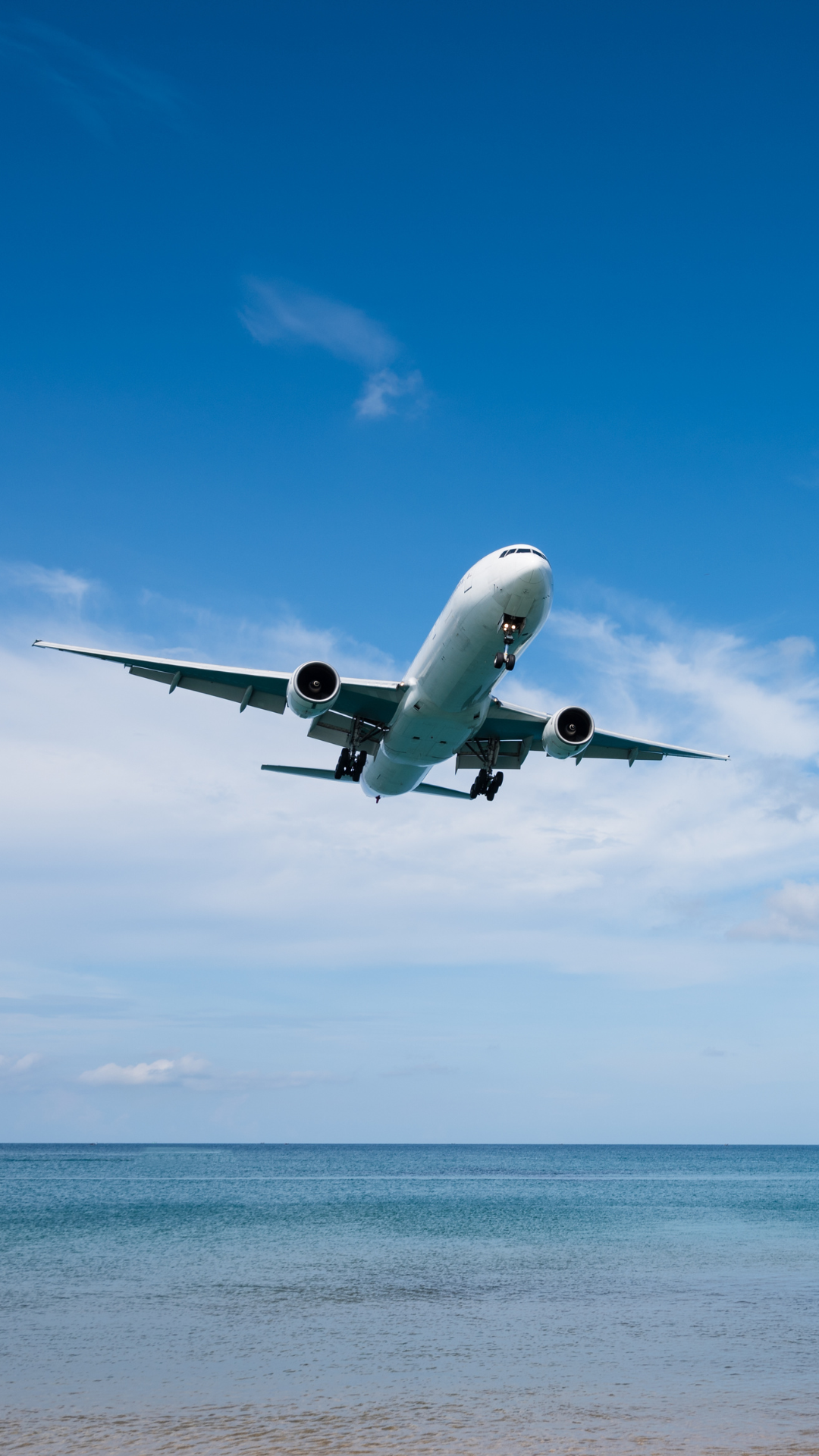 View below white airplane flying above the ocean on a clear day.