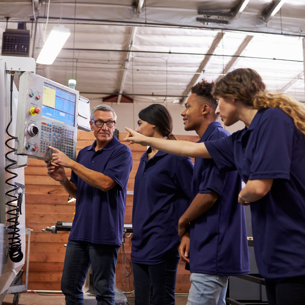 Three engineer training apprentices being trained by a superior regarding proper CNC machine usage  