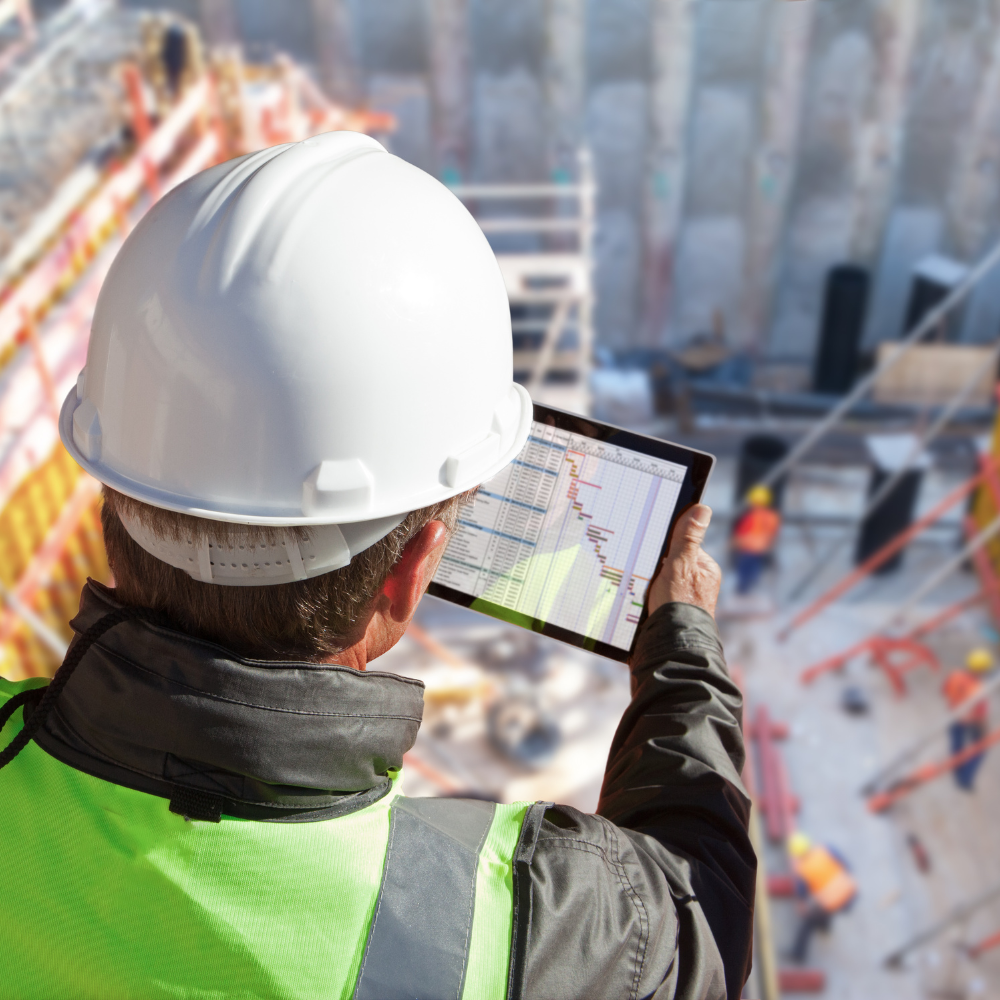 Caucasian male general contractor holding tablet displaying a gantt chart while overlooking an active construction site