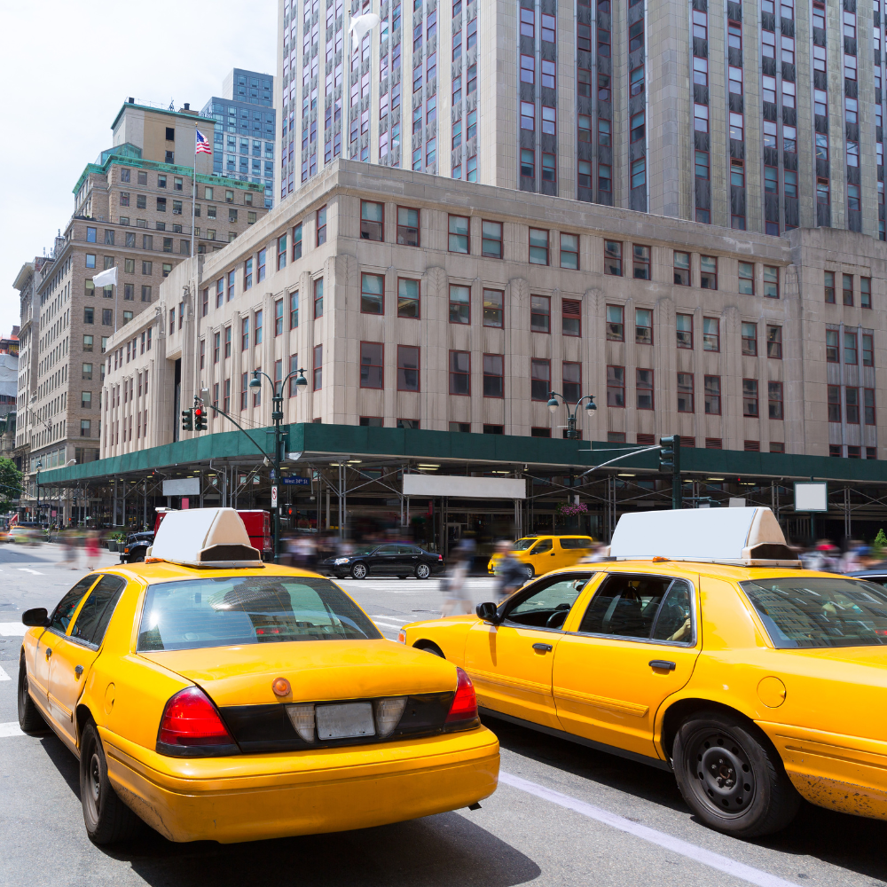 Two taxi cabs waiting at a red light in a busy intersection in a downtown area during the day